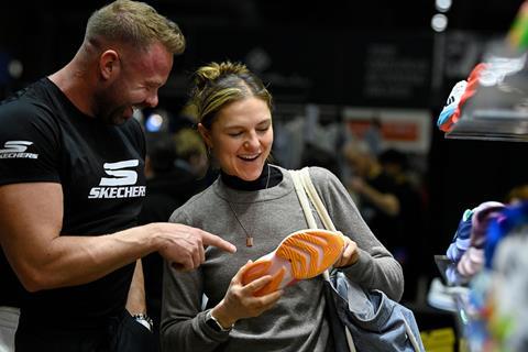 A woman smiles while a Skechers representative points out details on a running shoe she is holding.
